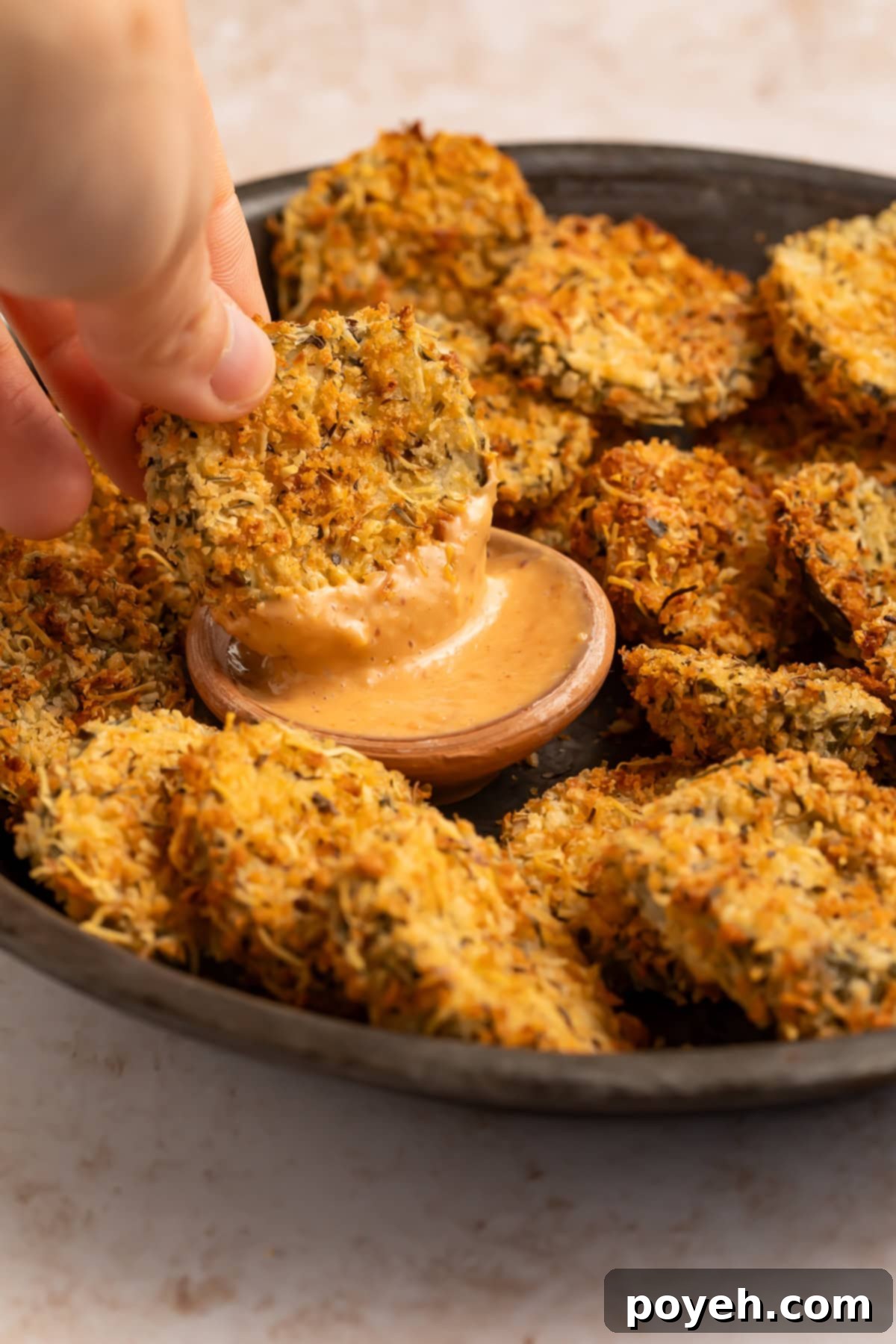 Fried pickle being dipped into a creamy, spicy sauce.
