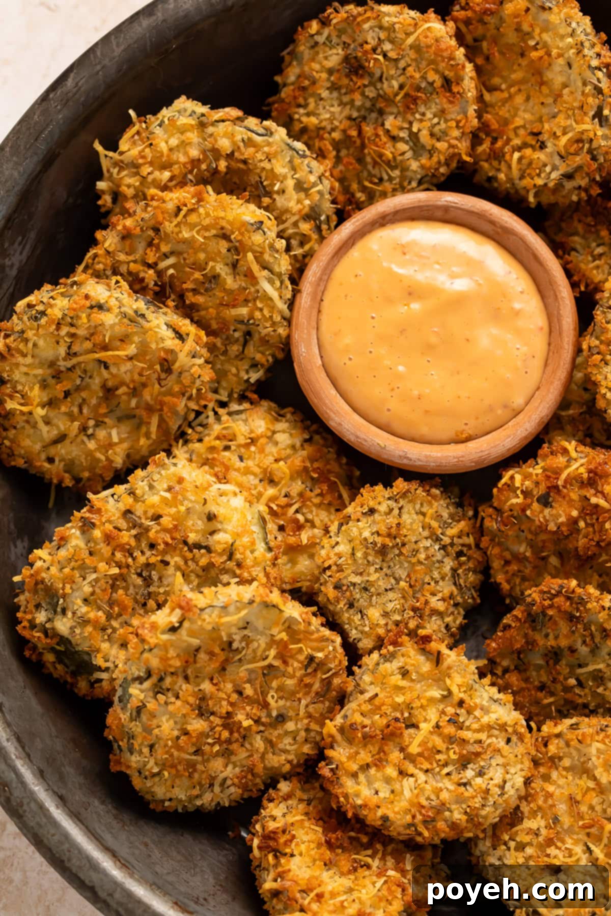 Close up of fried pickles in a black bowl with a small pot of spicy mayo for dipping.
