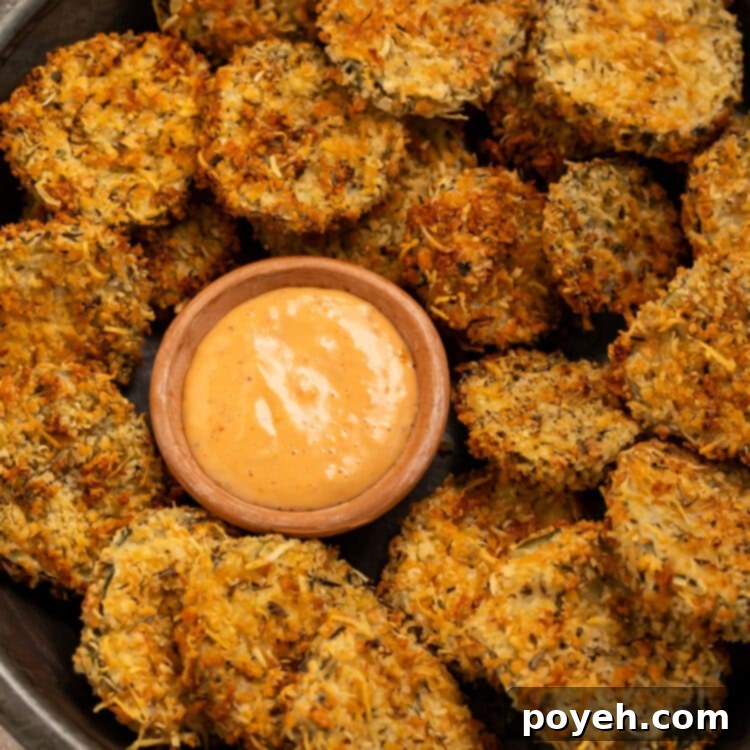 Black bowl of air fryer fried pickles with a small wooden bowl of creamy, spicy dipping sauce.