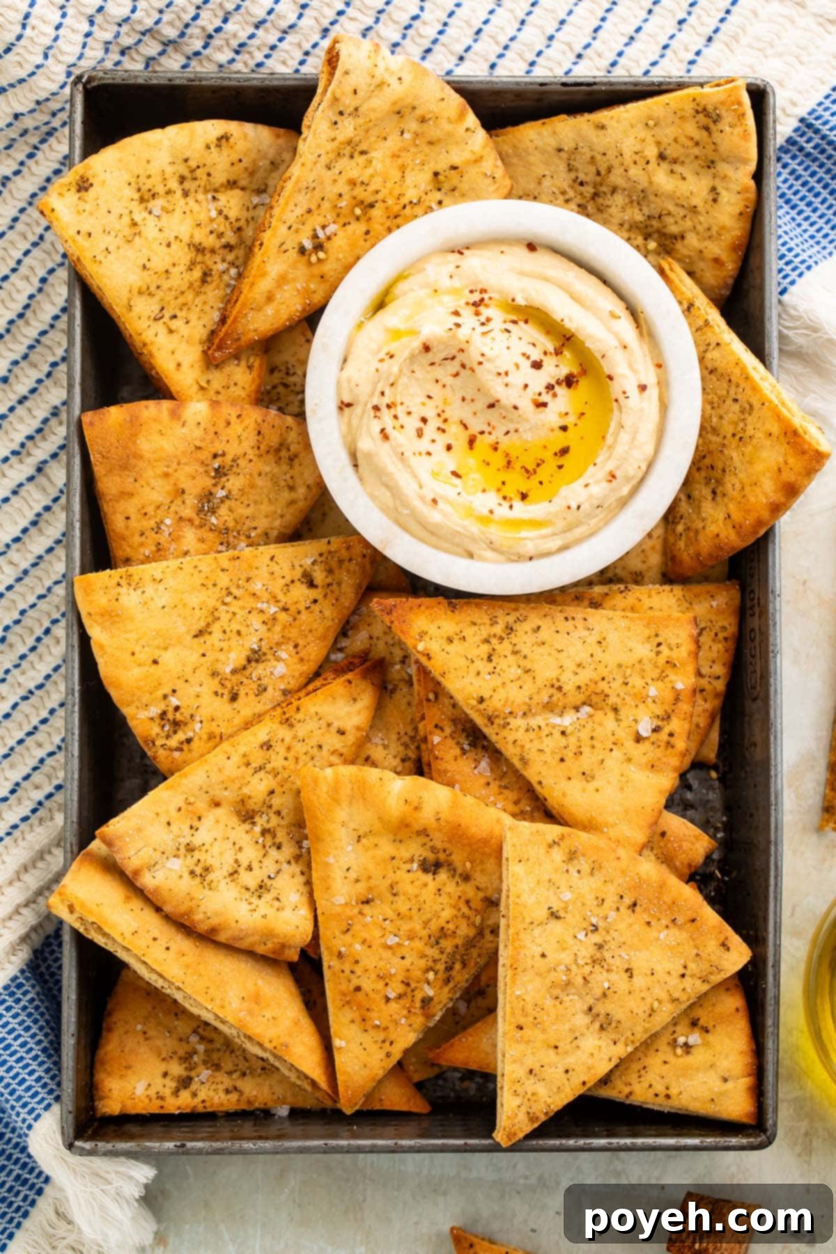 Homemade pita chips arranged neatly in a pan, with a small bowl of creamy hummus on the side, ready to be dipped and enjoyed.