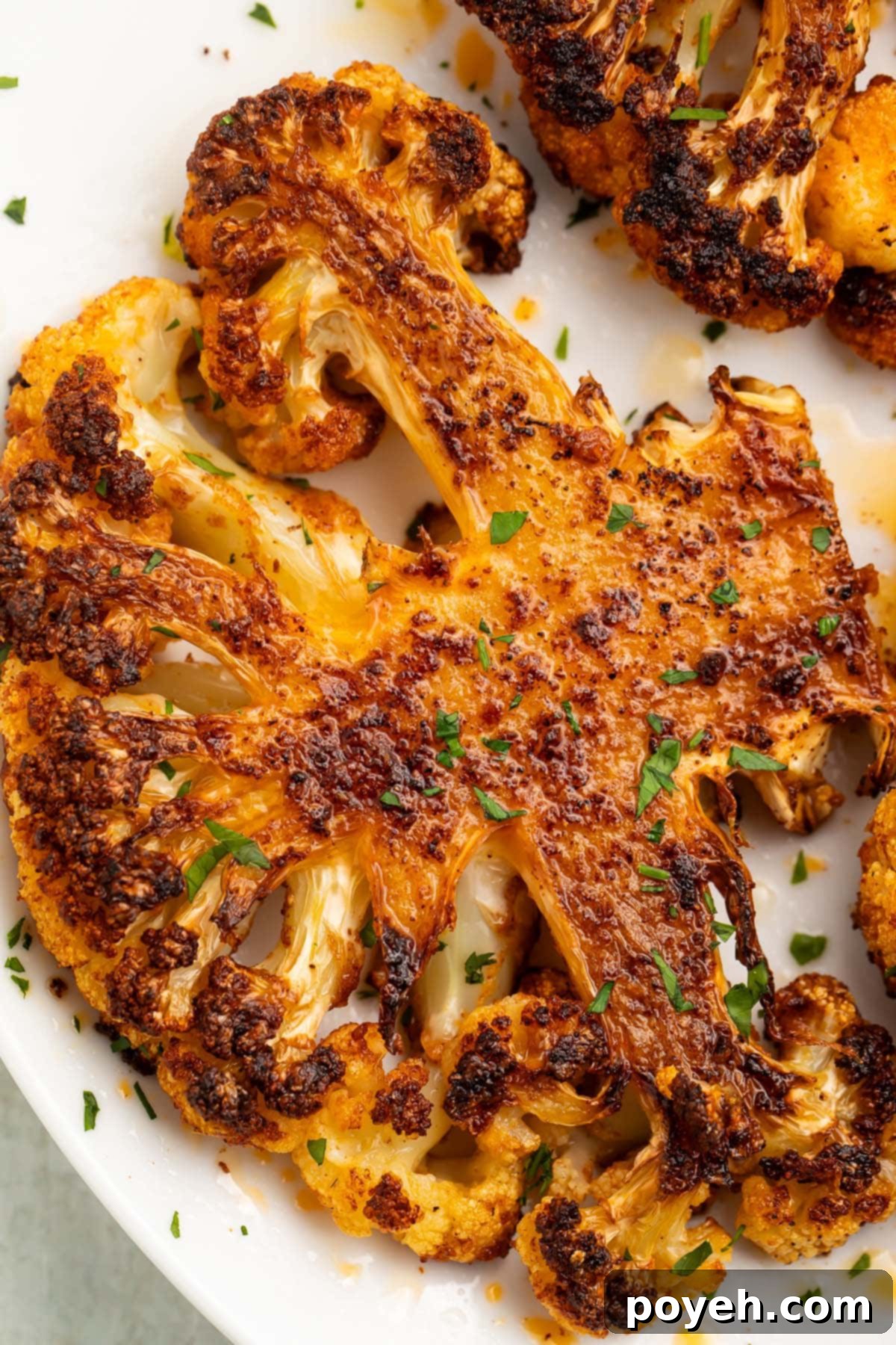 A perfectly roasted cauliflower steak on a pristine white plate, garnished with fresh herbs, showcasing its golden-brown crust and tender interior.