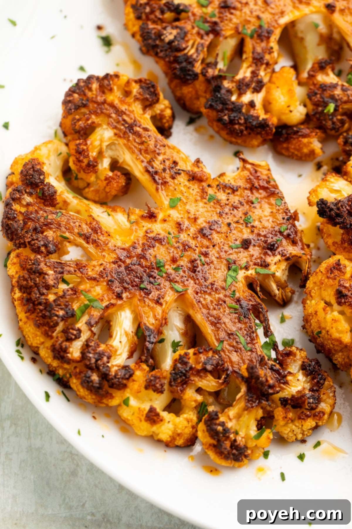 Another enticing view of a roasted cauliflower steak on a white plate, ready to be served, highlighting its appealing texture and seasoning.