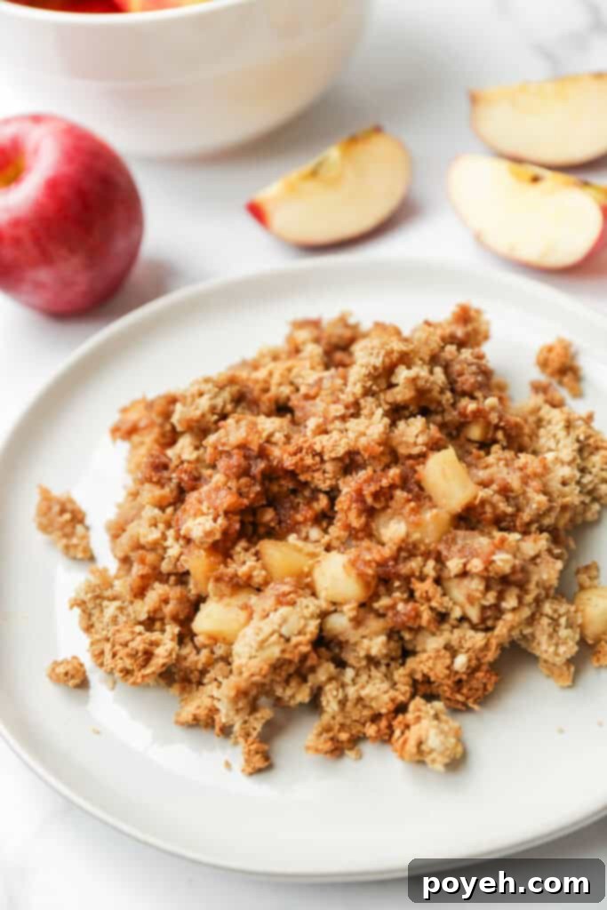 Cozy Vegan Apple Crumble 5 A close-up shot of a single serving of vegan apple crisp on a white plate, showcasing its golden brown, crunchy topping and warm apple filling.