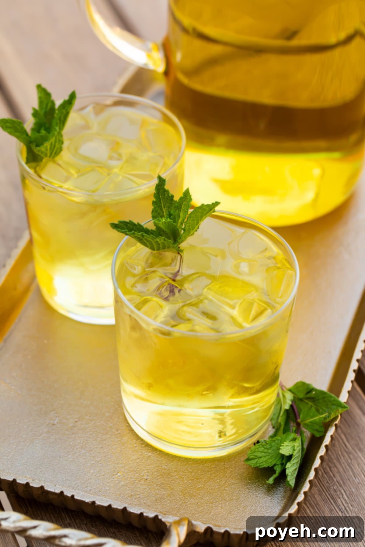 Close-up of a glass of cold brew green tea, showcasing the vibrant green hue and the subtle infusion of lemon slices and basil leaves within the drink.