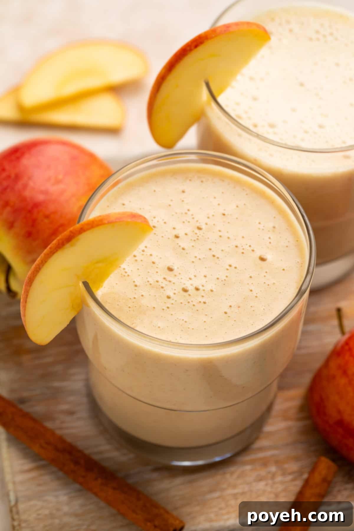 Close up of a pair of apple smoothies; the glasses are garnished with thin apple slices.