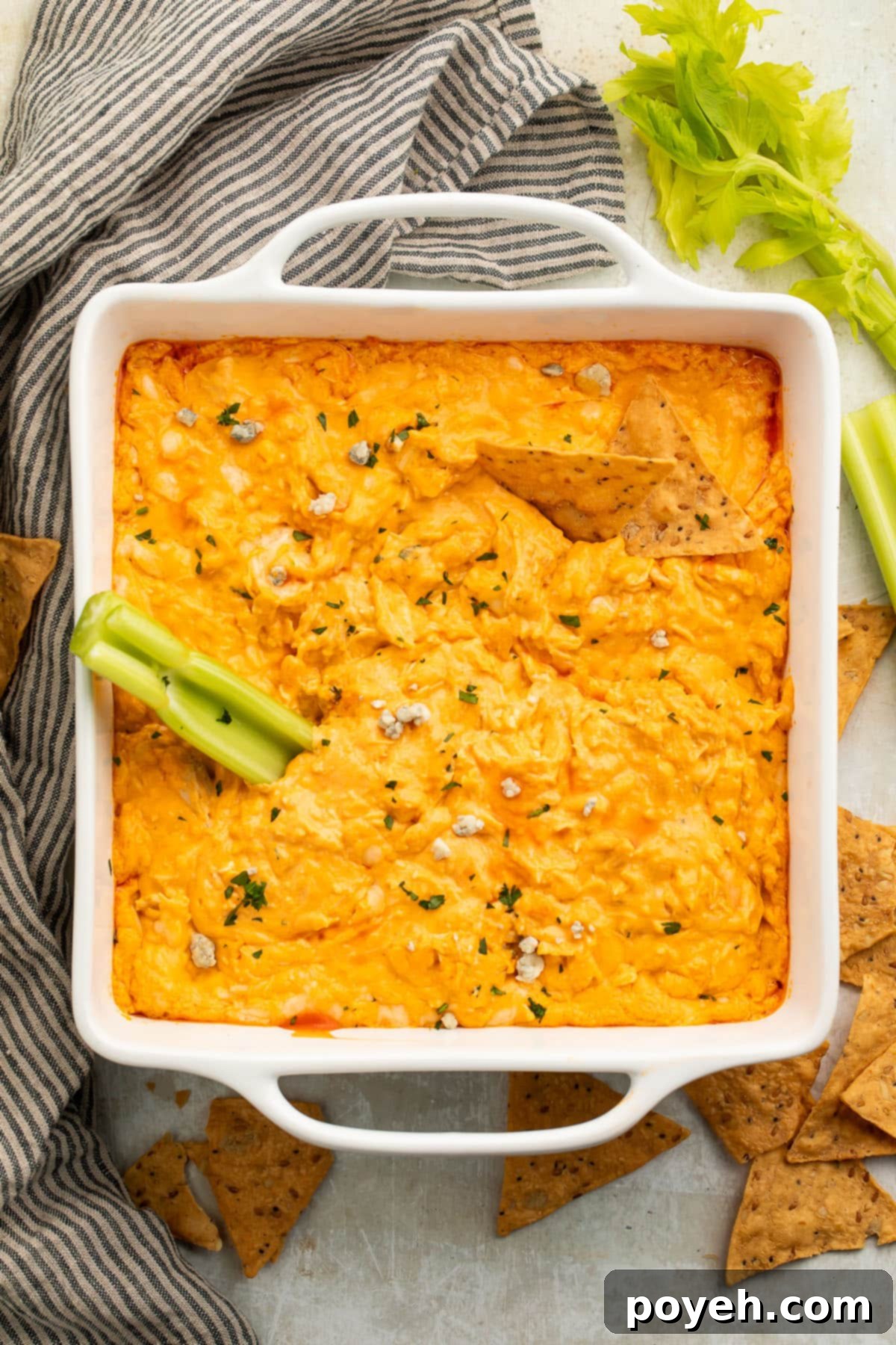A white square casserole dish filled with cheesy keto buffalo chicken dip, with a celery stick resting in the dip.