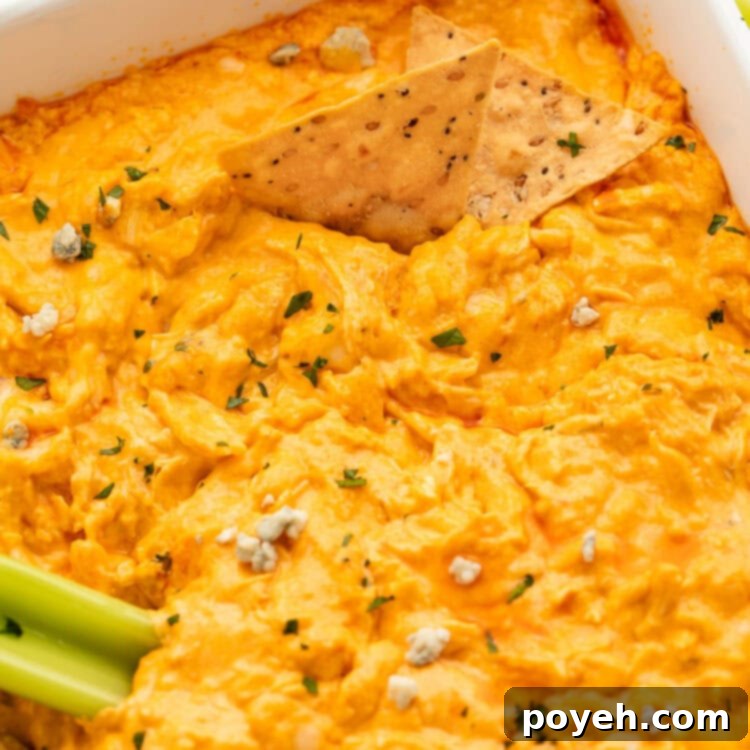A casserole dish holding keto buffalo chicken dip with a stick of celery and a tortilla chip resting in the dip.