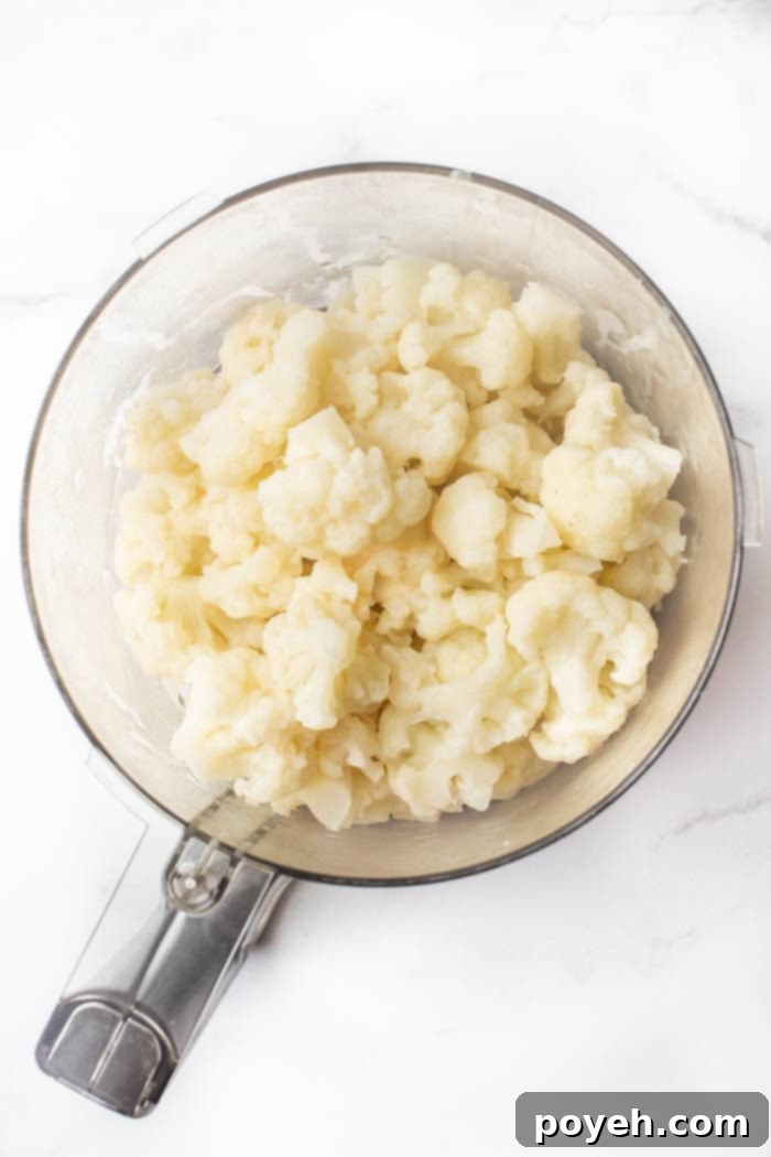 Steamed cauliflower being pulsed in a food processor to achieve a crumb-like texture, preparing it for chip formation.