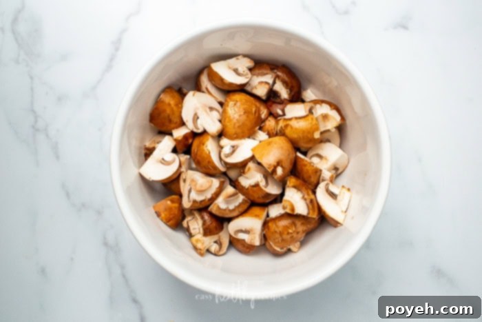 A white bowl full of uncooked and unseasoned mushrooms on a white counter
