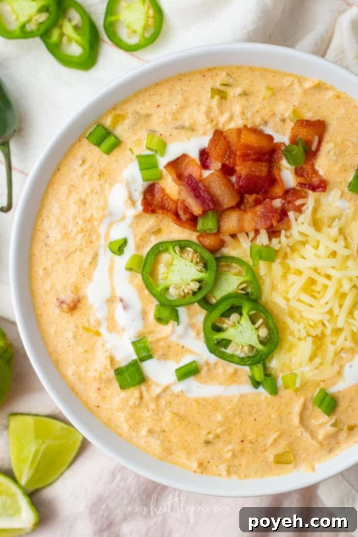 A steaming bowl of creamy keto white chicken chili, generously garnished with vibrant green jalapeno slices and crispy bacon bits, ready to be enjoyed as the ultimate comfort meal.
