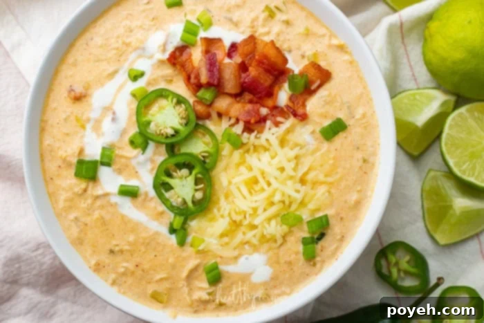 A perfectly prepared bowl of rich keto chicken white chili, beautifully topped with crispy bacon pieces and bright green jalapeno slices, accompanied by fresh lime wedges, ready for serving and enjoyment.