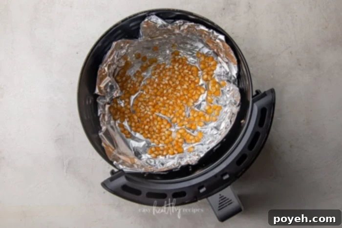 Popcorn kernels coated with oil and spread in a single layer on foil in an air fryer basket.