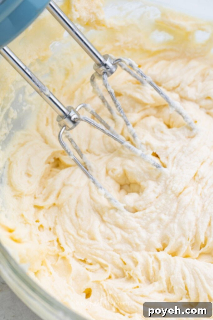 Keto cream cheese frosting being mixed in a large bowl with an electric mixer, showing its creamy texture.