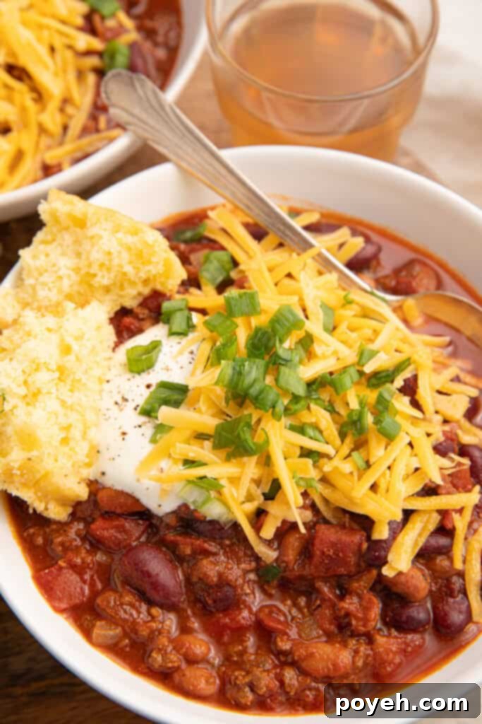 A bowl of bison chili in a white bowl topped with cheese and sour cream with a side of cornbread