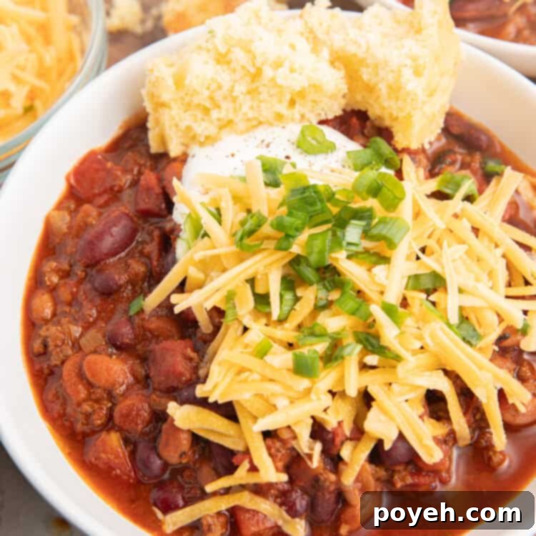 A bowl of bison chili with cornbread and topped with cheese and sour cream