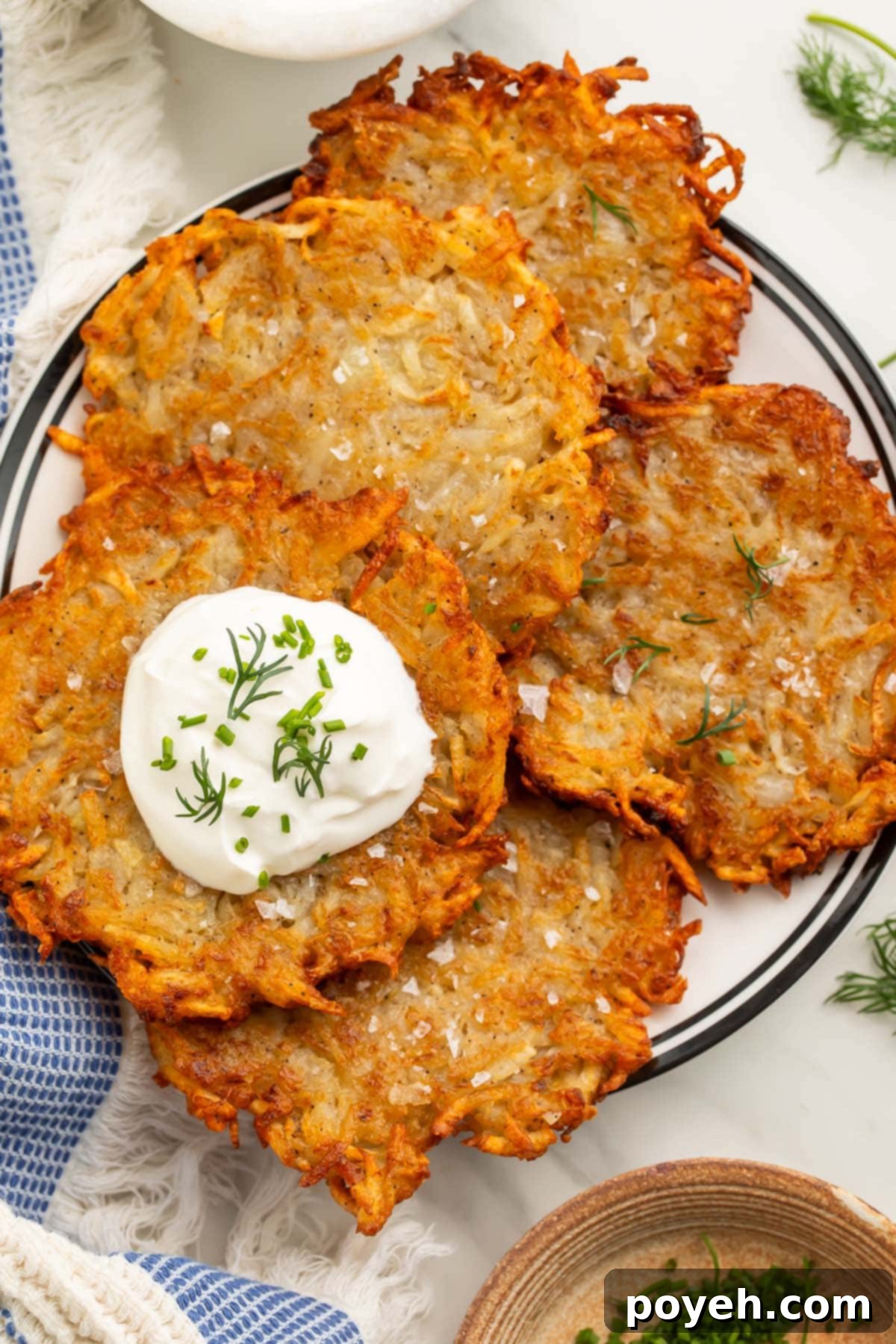 Four crispy dairy-free, vegan latkes piled on a plate and topped with vegan sour cream and chopped fresh dill.