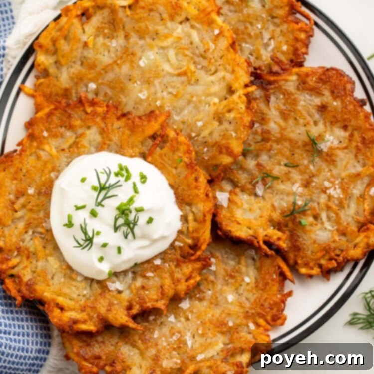 Four crispy dairy-free, vegan latkes piled on a plate and topped with vegan sour cream and chopped fresh dill.