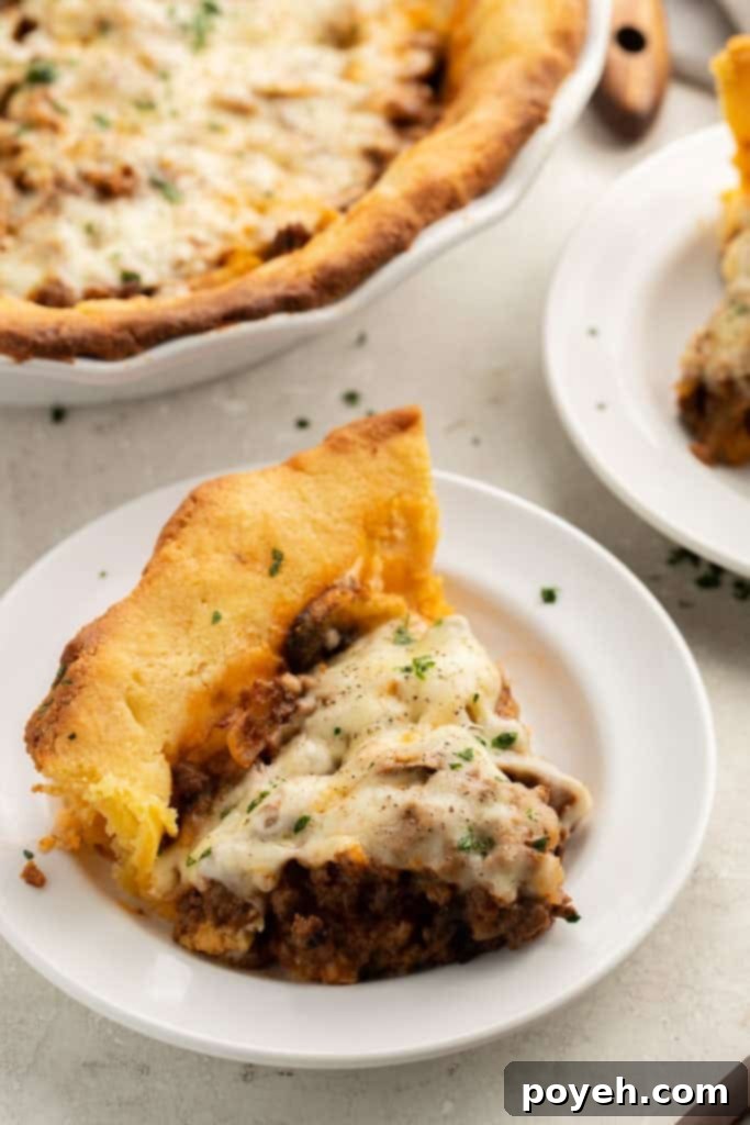 Pie slice of keto meat pie with ground beef, mushrooms, and mozzarella cheese on a white dish