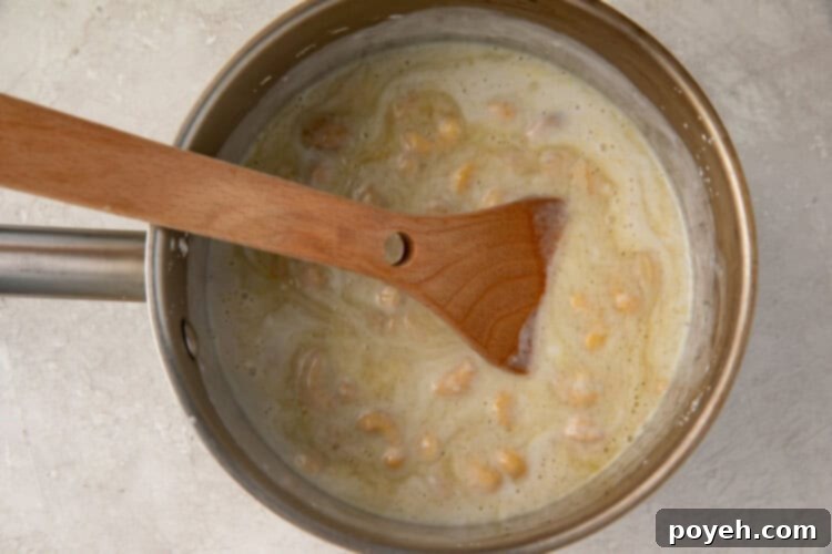The vegan crème brûlée base, enriched with sugar, vanilla, and a hint of turmeric, being stirred with a wooden spoon in a small saucepan.
