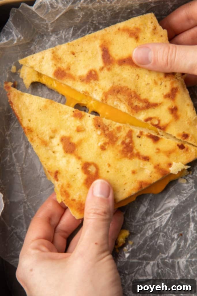 Two hands pulling apart slices of keto grilled cheese made with keto bread, revealing gooey melted cheese
