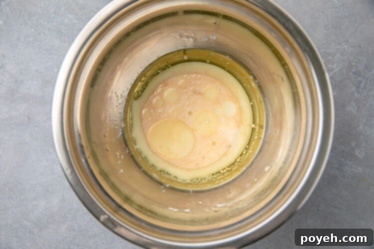 Gluten-Free Mug Cake Magic 4 Wet ingredients for gluten-free mug cake in a large silver mixing bowl, ready for dry ingredients to be added.