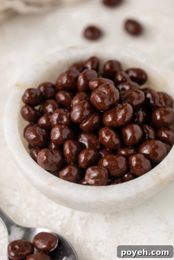 A close-up view of chocolate covered espresso beans artfully arranged in a small white bowl, showcasing their inviting texture.
