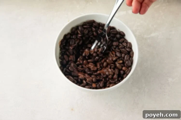 Espresso beans being stirred into a bowl of melted chocolate, ensuring full coverage.