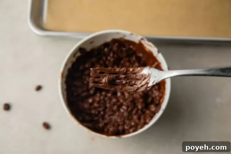 A chocolate covered espresso bean being placed on parchment paper with a fork, showing the careful separation process.