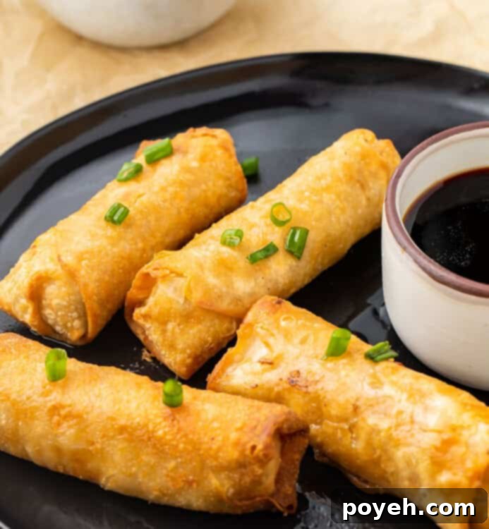 Crispy Air Fryer Frozen Egg Rolls 3 Four air-fried egg rolls perfectly arranged on a black plate with a small dish of soy sauce for dipping, showcasing their golden crispiness.