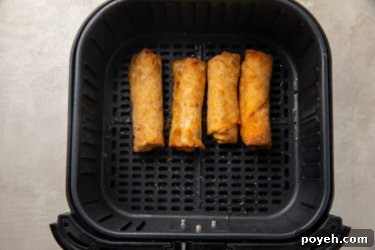 Crispy Air Fryer Frozen Egg Rolls 6 The same four frozen egg rolls, now partially cooked and flipped in the air fryer basket, with visible light browning on one side.