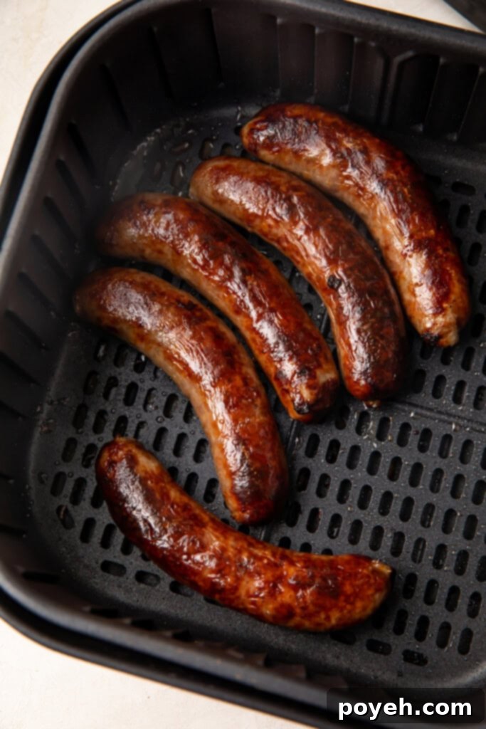 Perfectly cooked sausages resting in an air fryer basket, steam rising.