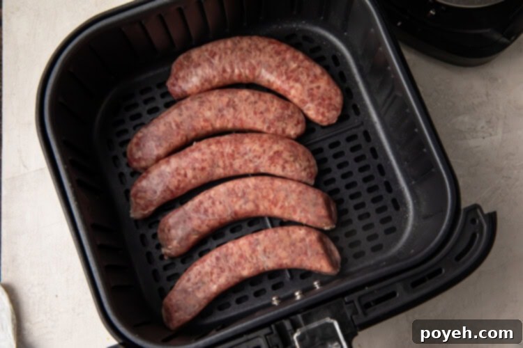 Uncooked sausages arranged in a single layer inside an air fryer basket.