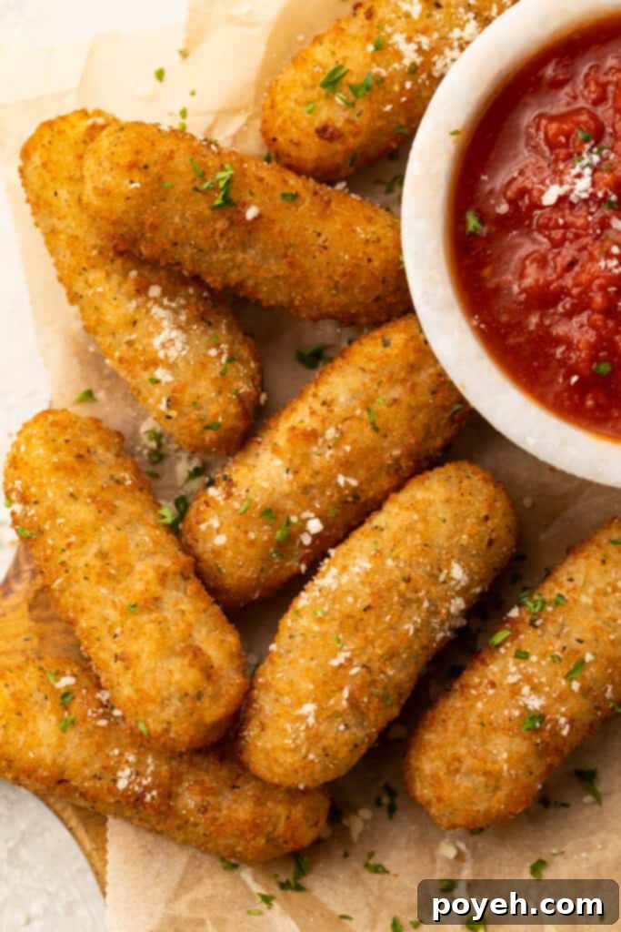 Frozen mozzarella sticks cooked in the air fryer then placed on a white plate with a small cup of marinara sauce