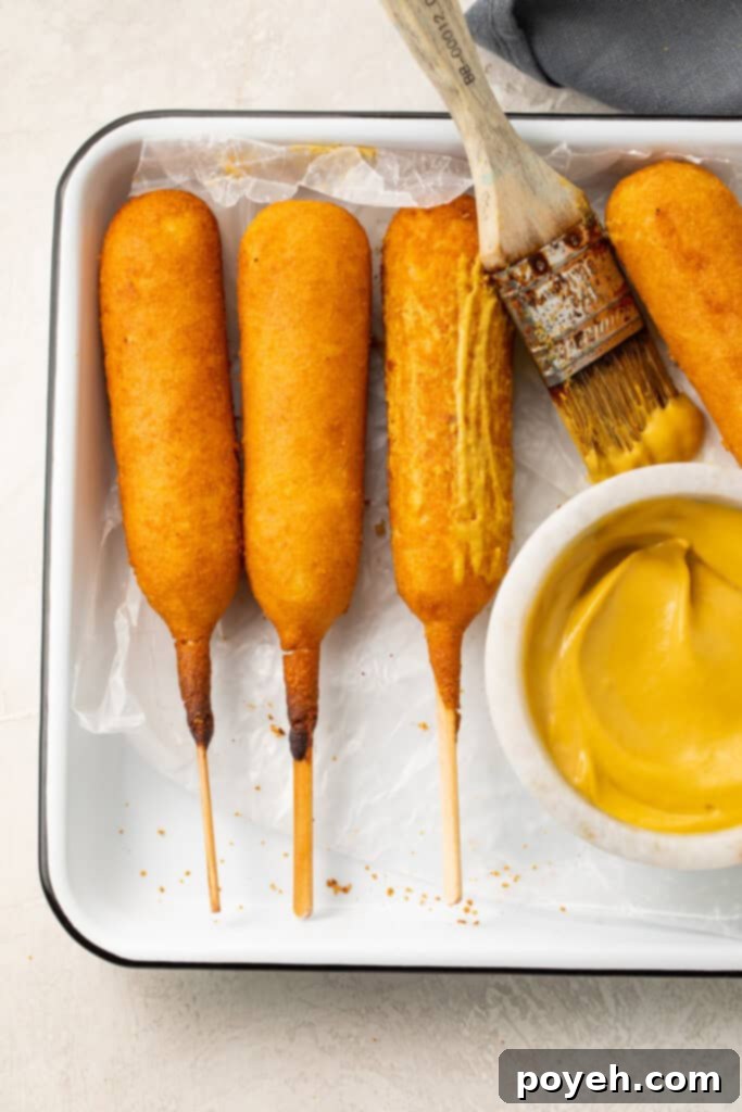 A serving of crispy air fryer corn dogs neatly arranged on a tray, accompanied by a small bowl of mustard for dipping.
