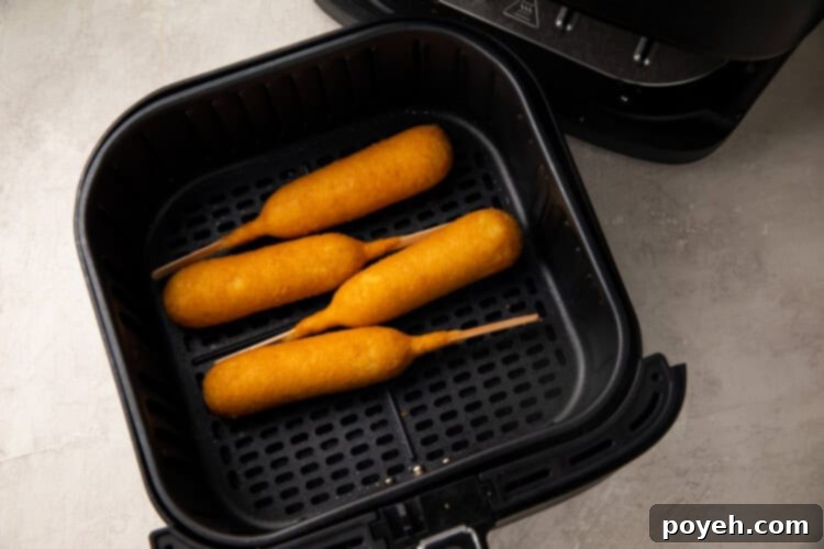 Corn dogs cooking in an air fryer basket, showing their golden-brown progress.