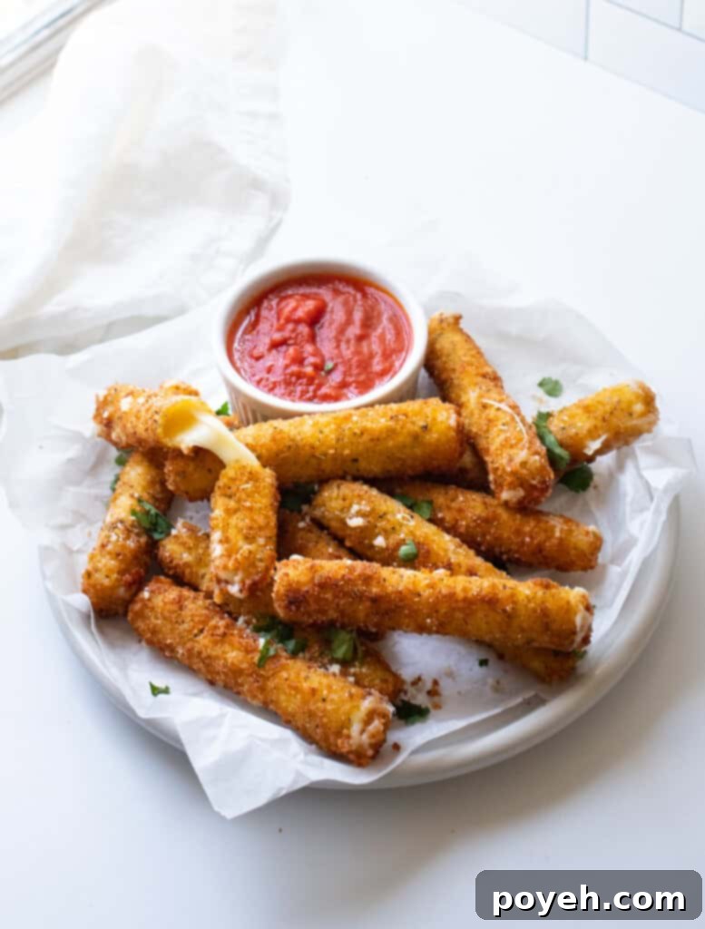 Gluten free mozzarella sticks on a white plate next to a dish of marinara sauce