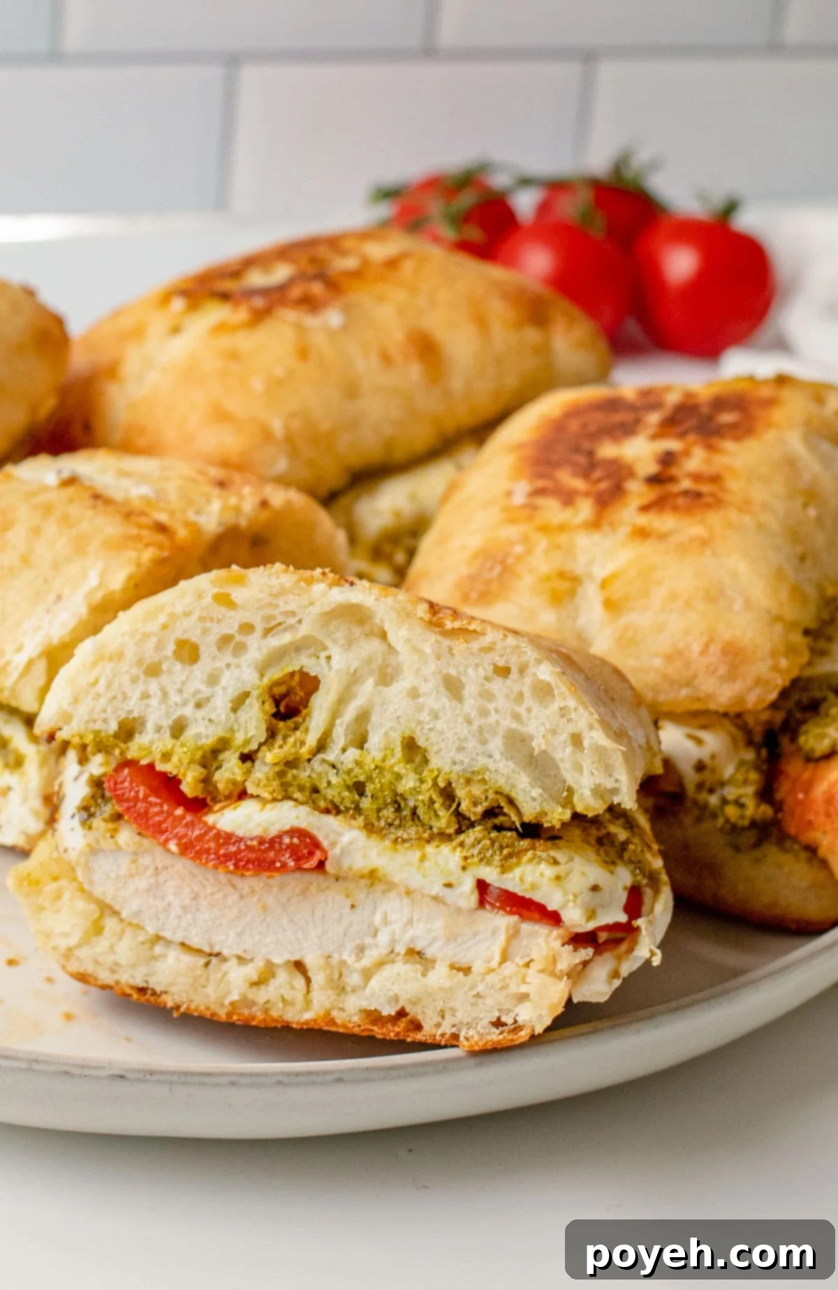 Cross section of a chicken pesto sandwich resting on the lip of a plate, with other sandwiches in the background.