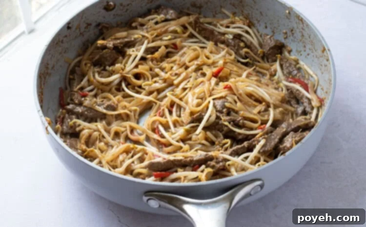 Beef pad thai with bean sprouts being stirred in a large skillet.