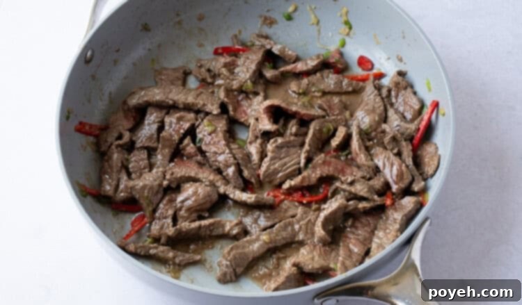 Thinly sliced beef cooking in skillet with garlic and red chilis.