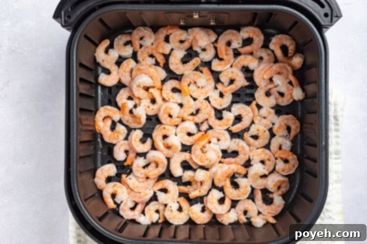 Shrimp cooking in an air fryer basket, halfway through.