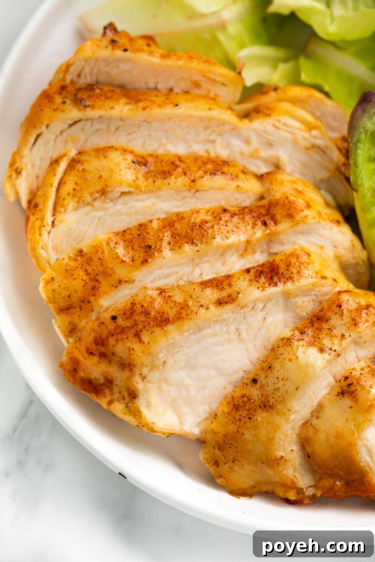 A previously frozen chicken breast that has been cooked in the air fryer, sliced, and arrange on a plate with a small salad.