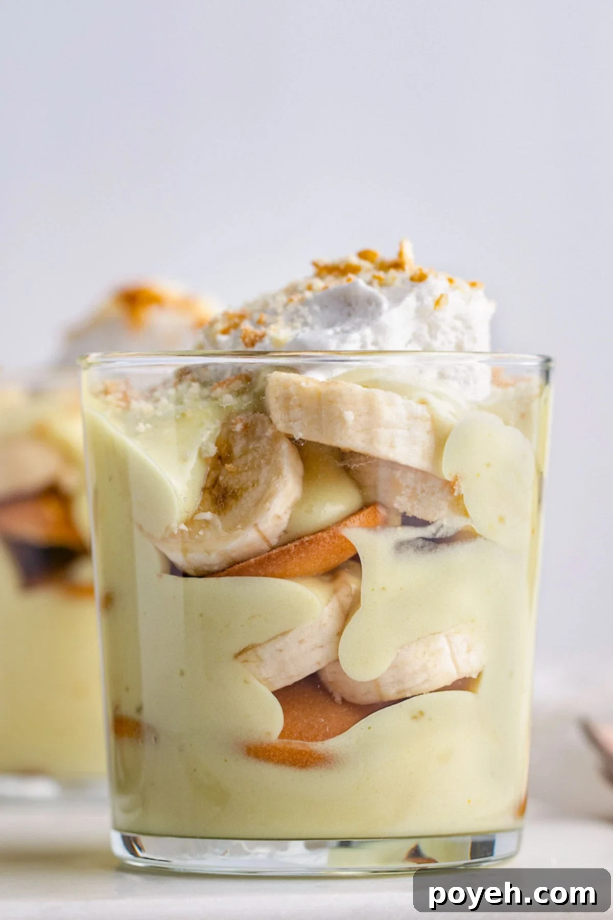 Side view of a short glass holding vegan banana pudding layered with slices of bananas and Nilla wafers.