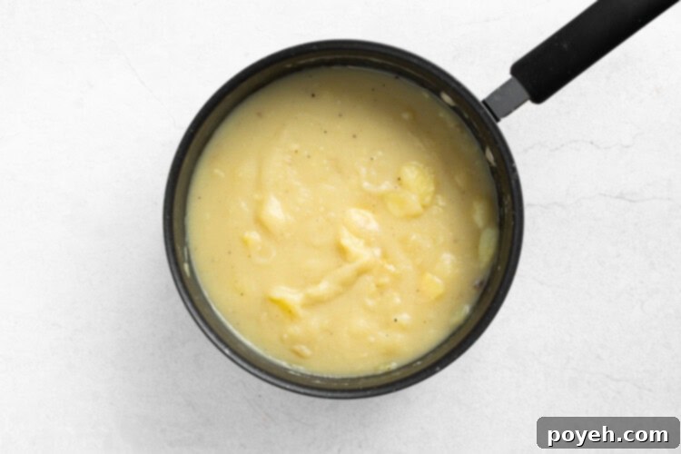 Step 3: Stewed potatoes boiling and reducing to a creamy consistency, being stirred.