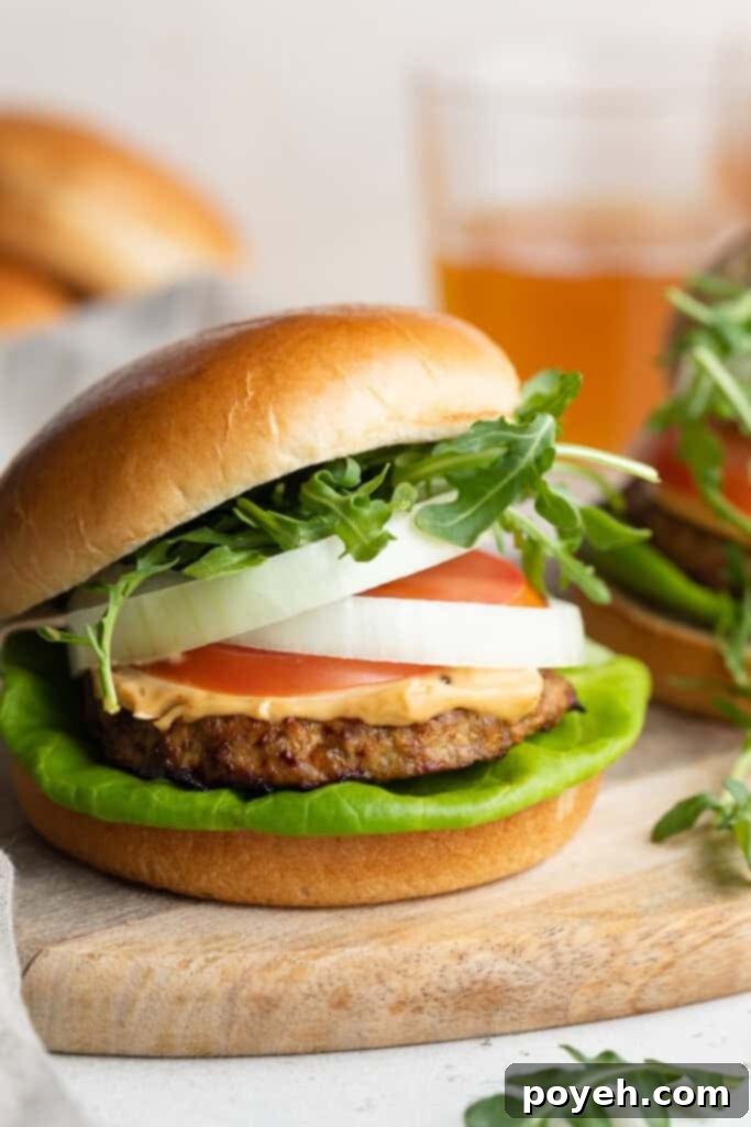 Close-up image of a succulent air fryer turkey burger, garnished with crisp lettuce, ripe tomato slices, red onion, a generous dollop of creamy chipotle mayo, and fresh arugula, served on a toasted bun.