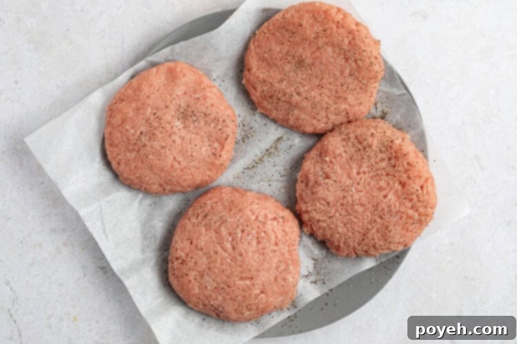 Pre-made turkey burger patties being seasoned with salt and black pepper.