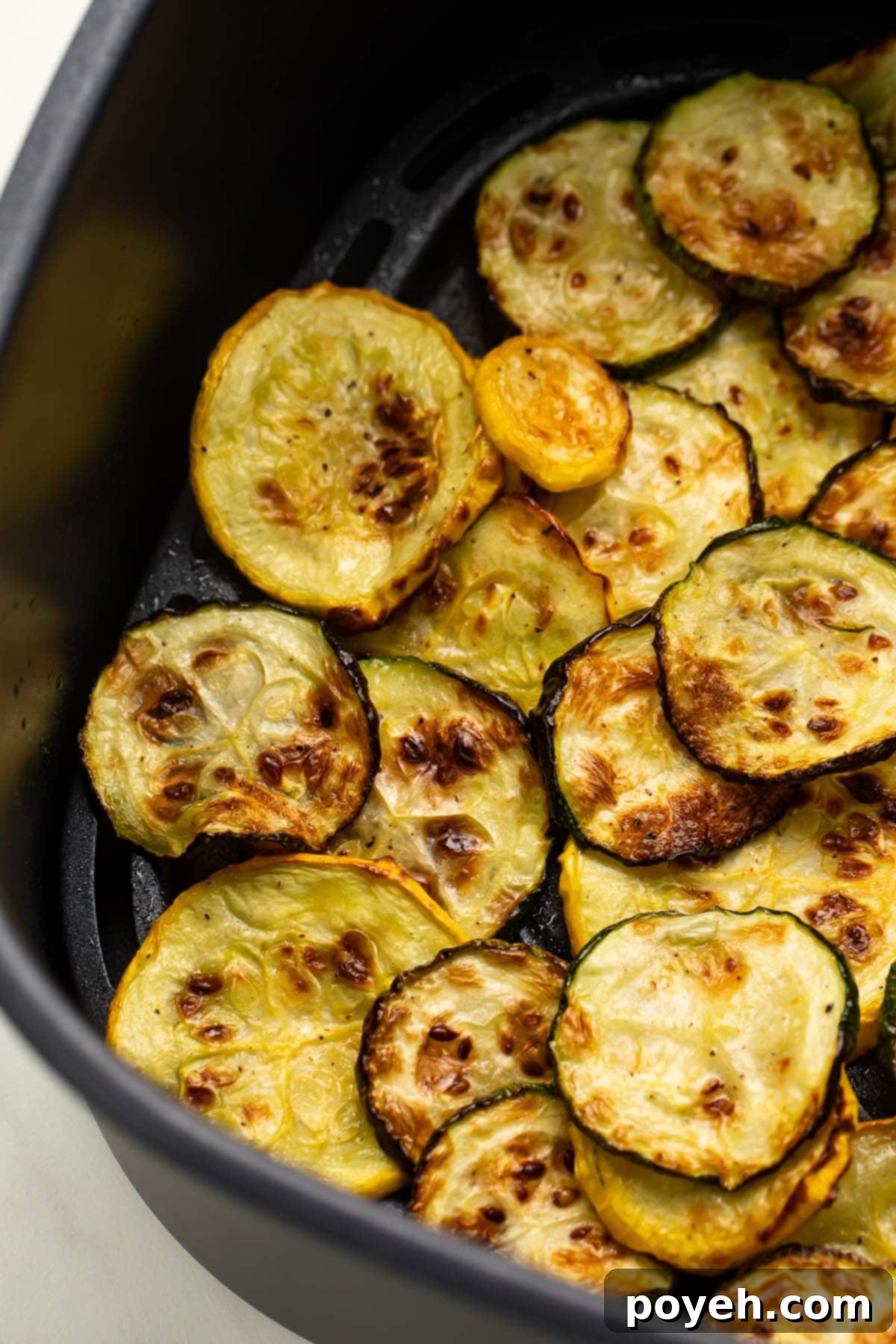 Close-up of golden-brown air fried yellow and green squash slices in an air fryer basket.