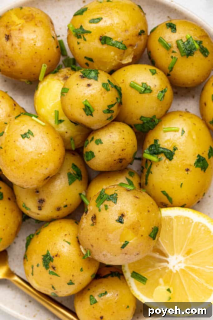 Overhead shot of steaming hot, buttery potatoes garnished with fresh herbs, served on a plate with a fork and lemon.