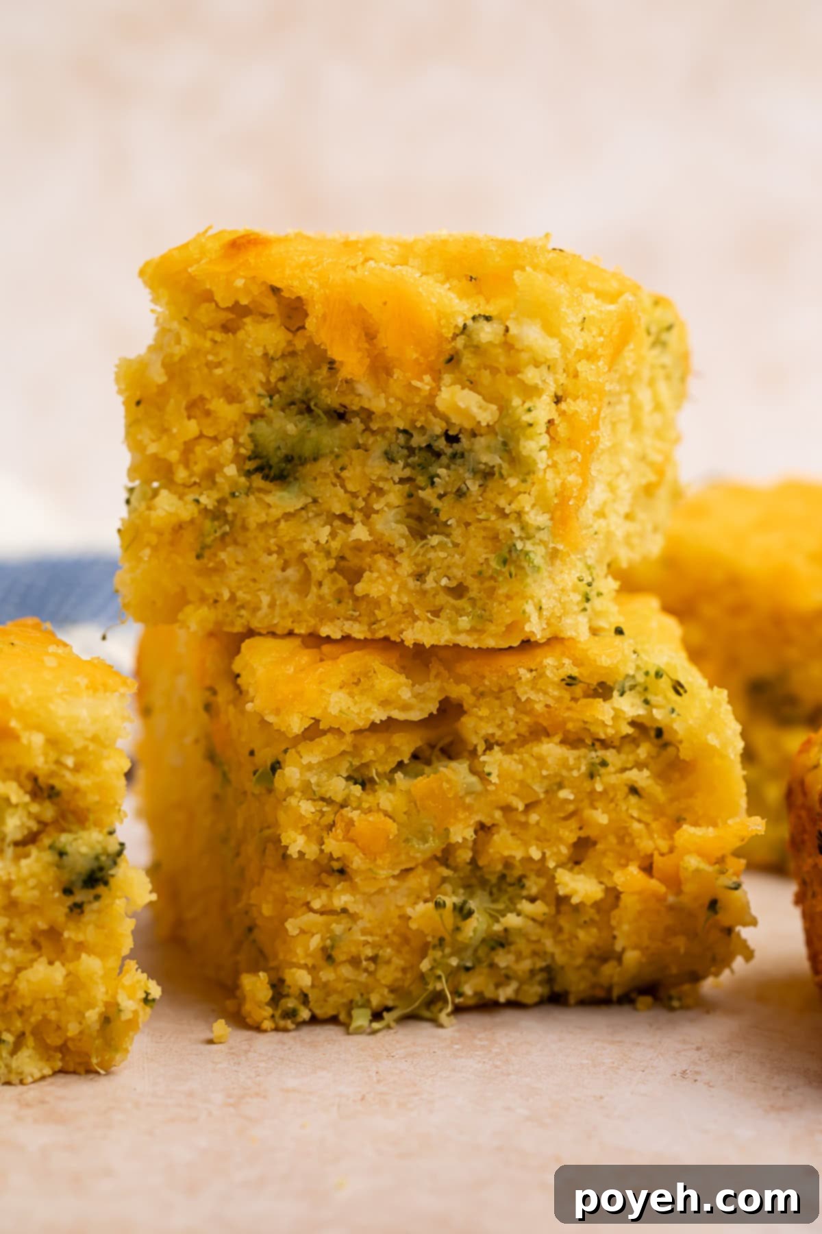Two golden-brown squares of cheesy broccoli cornbread, stacked elegantly one on top of the other, showcasing the vibrant green broccoli flecks within.