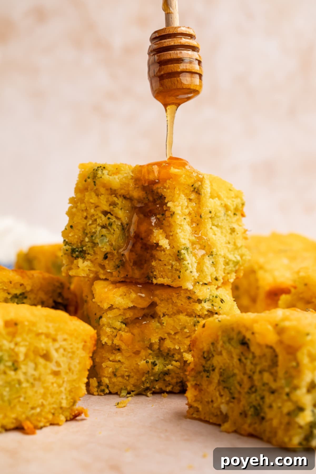 A stream of golden honey being delicately drizzled over two warm, stacked squares of broccoli cornbread, highlighting its moist interior.