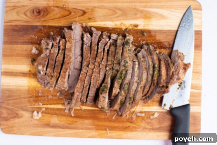 Perfectly cooked and sliced flank steak on a cutting board with a sharp knife